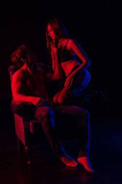 İç çamaşırlı seksi kadın striptiz yapan erkek arkadaş koltuğunda kırmızı ışıkta siyah ışıkta izole edilmiş.
