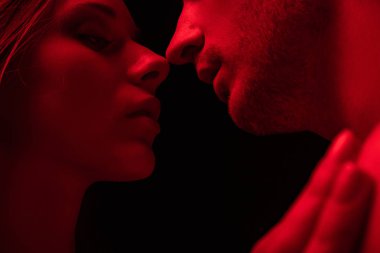 Kırmızı ışıkta öpüşen tutkulu seksi genç çift, siyahta izole edilmiş.