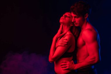Tutkulu çıplak adam siyah arka planda kırmızı ışıkta seksi genç kadına dokunuyor.