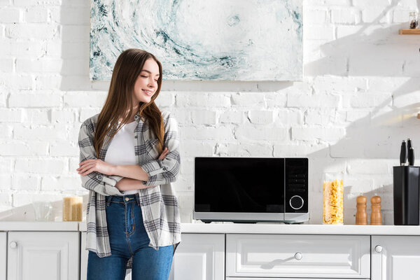 улыбающаяся и привлекательная женщина стоит рядом с микроволновой печью на кухне
 
