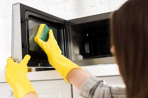 cropped view of woman in rubber gloves cleaning microwave with sponge