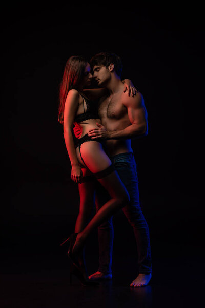 undressed sexy young couple kissing and hugging in red light isolated on black