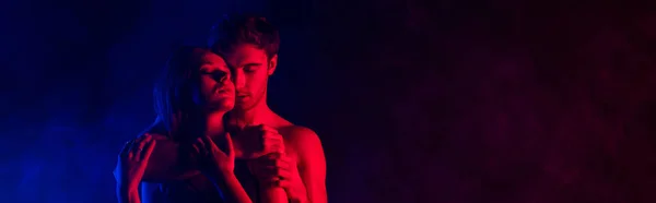 情熱的な服を着たセクシーな若いカップルが赤い光に抱きつきパノラマ撮影 — ストック写真