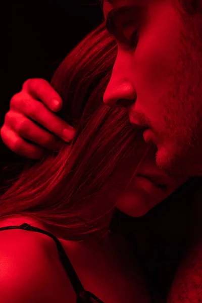 性感的年轻人 紧闭双眼 在深红色的光线下触摸着女孩的头发 与黑色隔离 — 图库照片