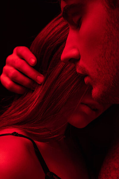 sexy young man with closed eyes touching girl hair in red light isolated on black