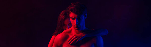 Naked passionate sexy young couple embracing in red and blue light on black background, panoramic shot