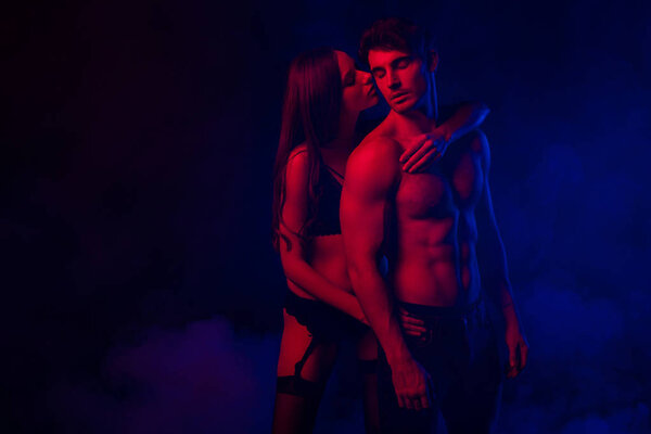 passionate undressed sexy young couple embracing in red and blue light on black background