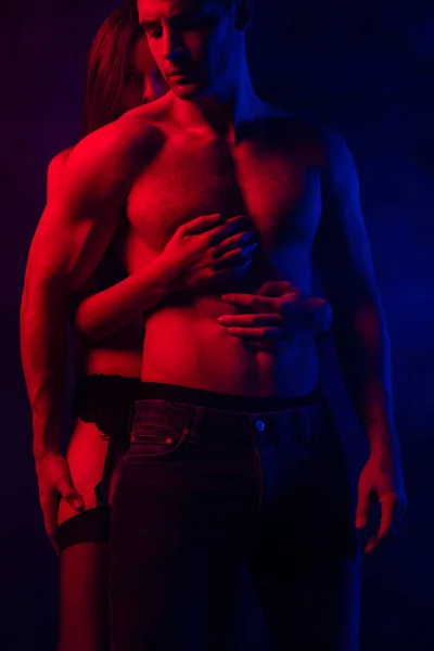 情熱的な服を着ていないセクシー若いカップル受け入れで赤と青の光上黒の背景 — ストック写真