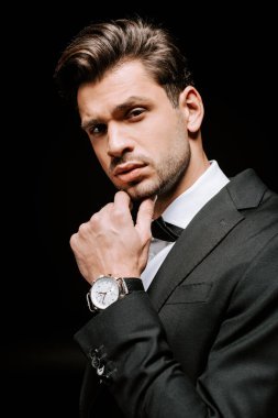 Yakışıklı bir adam siyah kameraya bakarken yüzüne dokunuyor. 