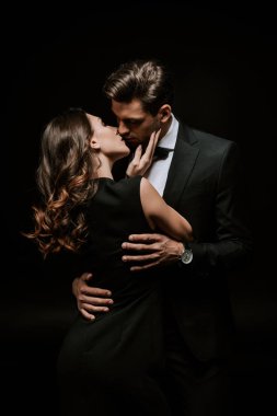 Güzel bir kadın siyah giyinmiş yakışıklı bir adamı öpüyor. 