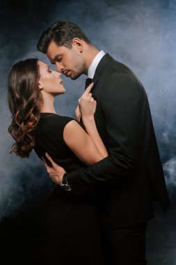 side view of man hugging attractive woman on black with smoke  clipart