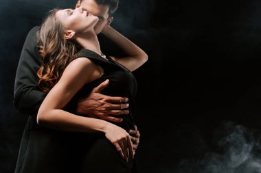 Takım elbiseli adam siyah giyinmiş seksi kadına dumanla sarılıyor. 
