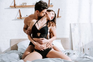Seksi üstsüz adam yatak odasında baştan çıkarıcı kızı öpüyor. 