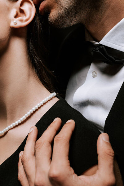 обрезанный вид мужчины, трогающего женщину с жемчужным ожерельем на шее
 