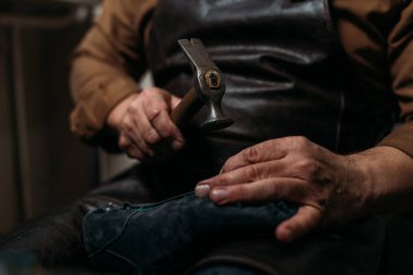 Atölyede ayakkabı tamir ederken elinde Hummer tutan ayakkabıcının kırpılmış görüntüsü