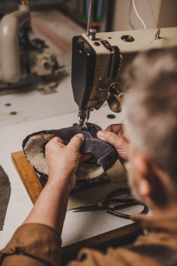 selective focus of cobbler sewing part of suede shoe on sewing machine clipart