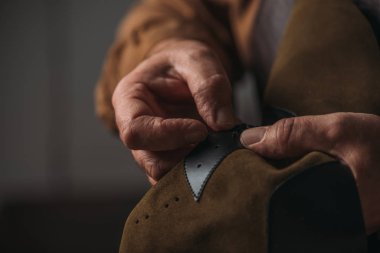 Kırpılmış ayakkabı tamircisinin elinde delikli bir deri parçası.