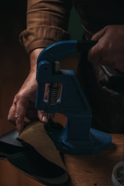 cropped view of shoemaker making holes in leather with puncher clipart
