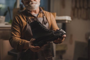 selective focus of cobbler showing handmade leather boot in workshop clipart