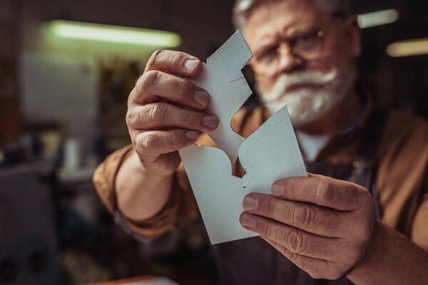 selective focus of senior cobbler holding templates for shoemaking in workshop