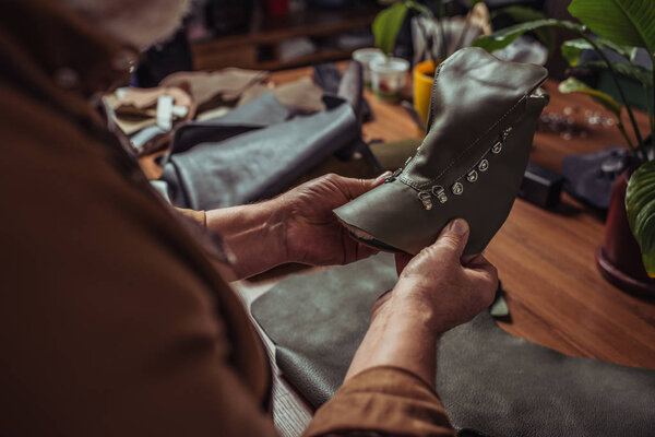 cropped view of shoemaker holding leather detail of unfinished shoe in workshop