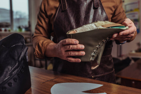 cropped view of cobbler holding leather detail of unfinished shoe in workshop