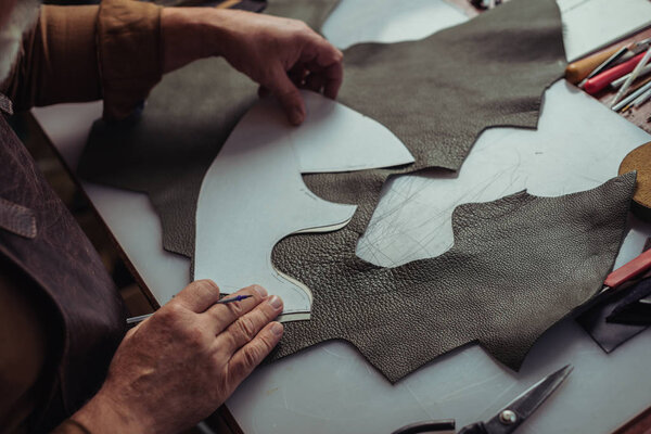 cropped view of cobbler holding piece of leather near template in workshop