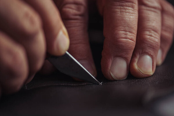cropped view of shoemaker cutting genuine leather with knife