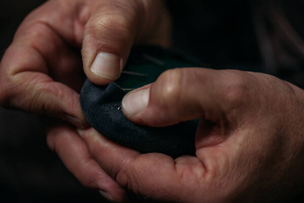 cropped view of shoemaker fixing leather to shoe in workshop