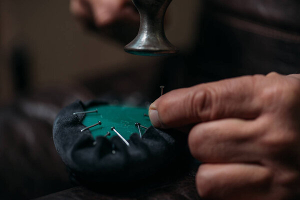 cropped view of cobbler fixing leather to shoe with nails in workshop