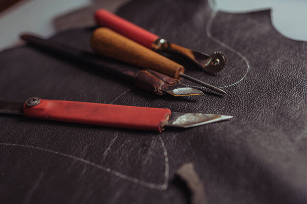 selective focus of cutters, awl and tracing wheel on genuine leather in workshop