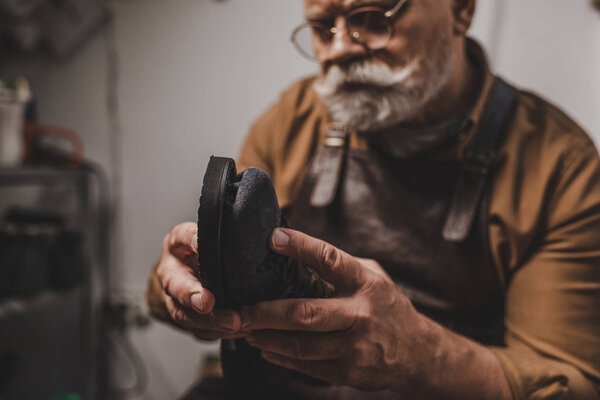 selective focus of senior cobbler repairing shoe in workshop