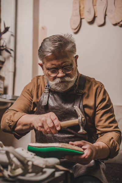 старший, бородатый сапожник ремонта обуви с хаммером в мастерской
