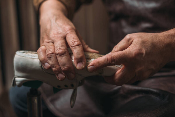 cropped view of shoemaker repairing shoe in workshop