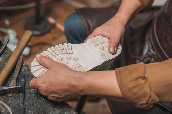 cropped view of shoemaker fixing sole to boot in workshop