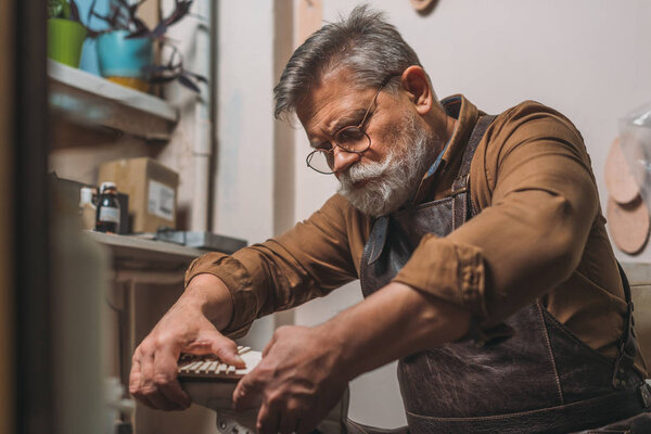 selective focus of senior cobbler fixing sole to shoe in workshop