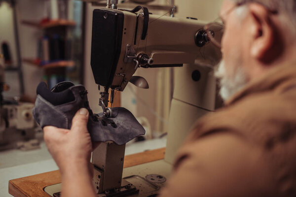 selective focus of cobbler sewing part of suede shoe on sewing machine