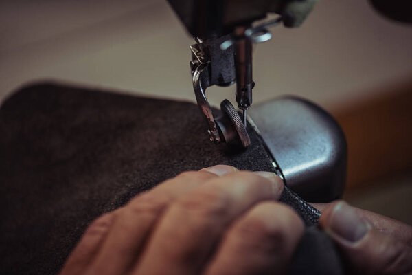 partial view of shoemaker sewing genuine leather on sewing machine