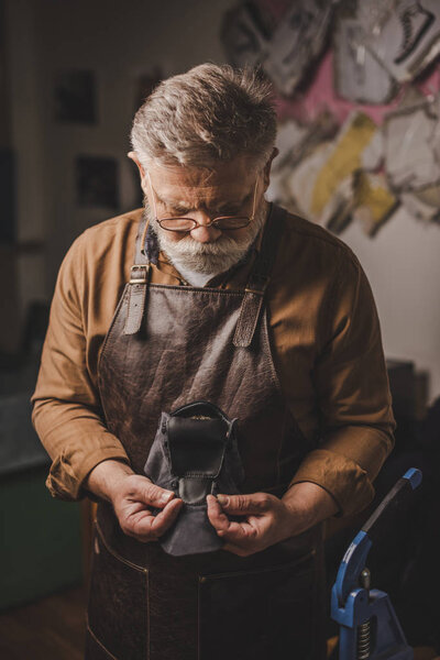 attentive, senior cobbler holding leather detail in workshop