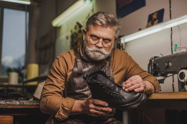 Seriöser Älterer Schuhmacher Mit Lederstiefeln Vor Der Kamera — Stockfoto
