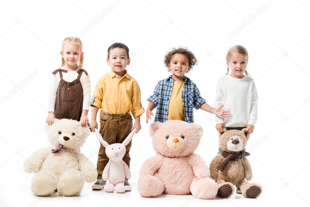 happy multicultural kids standing with teddy bears and bunny toy