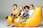 adorable multicultural kids sitting on bin bag chair on grey