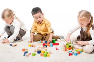 çok kültürlü çocuklar halının üzerinde tahta bloklarla oynuyorlar, beyazlar üzerinde izole edilmiş.