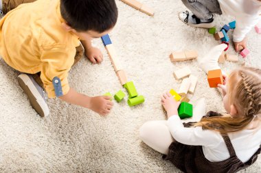 top view of children playing with wooden blocks on carpet clipart