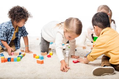 Çok ırklı çocuklar halının üzerinde tahta bloklarla oynuyorlar, beyazlar üzerinde soyutlanıyorlar.