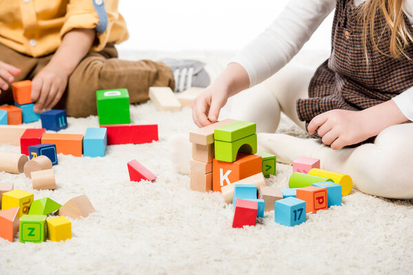 cropped view of children playing with wooden blocks on carpet