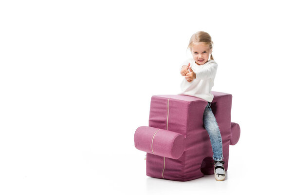 happy kid showing thumbs up on purple puzzle chair, isolated on white 