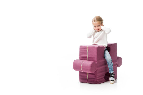 kid closing ears while sitting on purple puzzle chair, isolated on white 