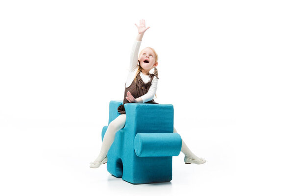 excited child sitting on blue puzzle chair, isolated on white 