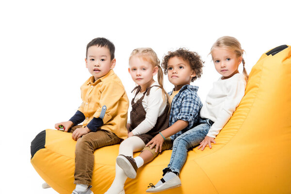 cute multicultural kids sitting on bin bag chair isolated on white